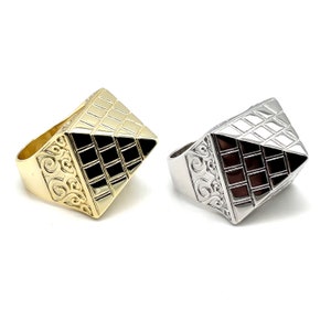 Può includere: Due anelli geometrici con un design a forma di piramide. Un anello è in oro con una piramide nera, l'altro è in argento con una piramide marrone.