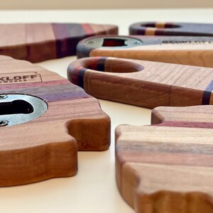 May include: A set of four wooden bottle openers, each with a unique shape and design. The openers are made from different types of wood, including maple, walnut, and cherry. The openers are all finished with a clear coat to protect the wood. The openers are all engraved with the words "Beckloff Woodworks".