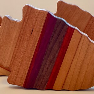 May include: Three wooden arrowhead-shaped cutting boards with a layered design of different wood types, including cherry, maple, walnut, and purpleheart. The boards are arranged in a staggered formation.