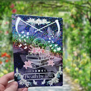 May include: A holographic sticker with a skull, books, and flowers. The sticker has the text "Death by TBR" on it.