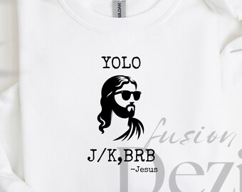 May include: White sweatshirt with a black graphic of Jesus wearing sunglasses, the word "YOLO" above the graphic, and the text "J/K, BRB -Jesus" below. The sweatshirt is made of a soft material.
