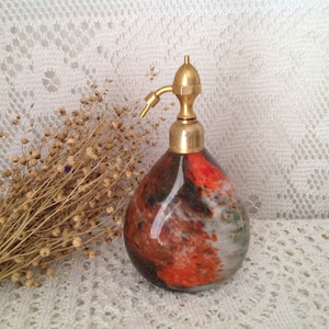 May include: A vintage glass atomizer bottle with a brass pump and a colorful abstract design in shades of orange, black, and white.