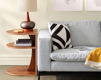 Può includere: Un divano grigio chiaro con una coperta color giallo senape e due cuscini geometrici bianchi e neri. Ai lati del divano ci sono due tavolini in legno, ciascuno con una lampada con paralume beige e base scura. Tre stampe astratte incorniciate.