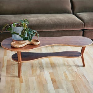 May include: A two-tiered coffee table with a unique, organic shape. The table is made of wood with a dark brown stain and has a natural wood grain pattern. The table is sitting on a light wood floor.