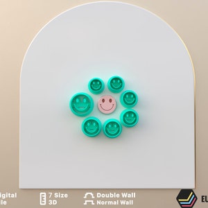 May include: A set of seven turquoise blue smiley face cookie cutters, arranged in a circle around a single pink smiley face cookie cutter.