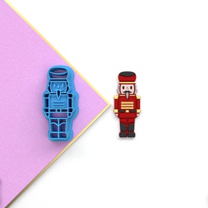 May include: A blue plastic cookie cutter shaped like a nutcracker, and a red plastic nutcracker figurine.