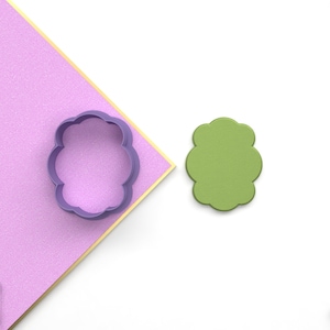 May include: Purple plastic cookie cutter shaped like a flower, next to a green plastic flower-shaped cookie cutter.