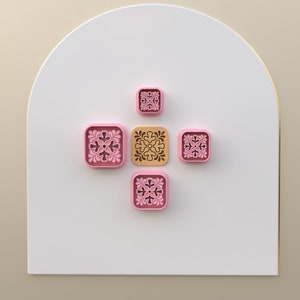Puede incluir: Cinco azulejos decorativos con intrincados diseños florales. Cuatro azulejos son de color rosa con un patrón floral blanco, y un azulejo es de color beige con un patrón floral marrón.