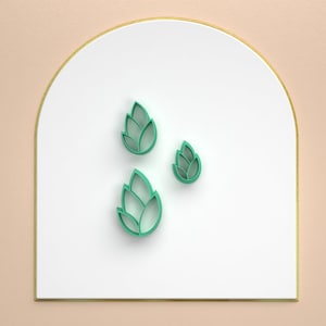 May include: Three green paper cutouts of stylized leaves on a white background with a gold border.