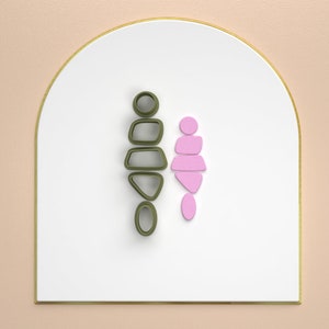 Op de afbeelding: Een set gestapelde geometrische vormen, een in groen en een in roze, op een witte achtergrond met een gouden rand.