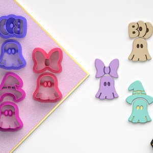 Op de afbeelding: Set van negen Halloween-thema koekjesuitstekers. De uitstekers zijn gemaakt van plastic en hebben verschillende ontwerpen, waaronder geesten, heksen, strikken en de woorden "BOO" en "BOO!" De uitstekers zijn roze, paars, lichtblauw en beige.