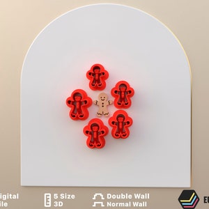 Puede incluir: Un juego de seis cortadores de galletas de jengibre rojo en forma de hombre, con un cortador en el centro de color marrón claro.