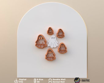 Pode incluir: Conjunto de seis cortadores de biscoitos em forma de fantasmas. Cinco são laranja e um é branco. Os cortadores estão dispostos em uma superfície branca.