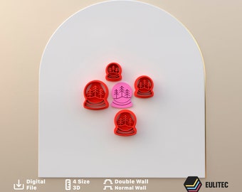 Puede incluir: Conjunto de cinco cortadores de galletas de color rojo y rosa con forma de bola de nieve con árboles en su interior. Los cortadores están dispuestos en círculo sobre una superficie blanca.