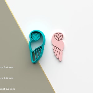 May include: Two owl cookie cutters, one teal blue and one pink. The teal blue owl is facing left and the pink owl is facing right. Both owls have a heart-shaped head and wings.