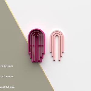 Op de afbeelding: Twee boogvormige koekjessnijders, één magenta en één lichtroze, worden weergegeven op een witte en grijze achtergrond. De magenta snijder heeft een gedetailleerder ontwerp. De afbeelding bevat ook tekst en pictogrammen die de beschikbaarheid van het STL-bestand aangeven.