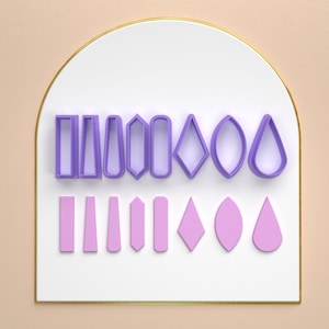 Może przedstawiać: Zestaw 12 fioletowych plastikowych foremek do ciasteczek w różnych kształtach, w tym prostokąty, owale, diamenty i kształty łezki. Formy są ułożone w dwóch rzędach na białym tle.