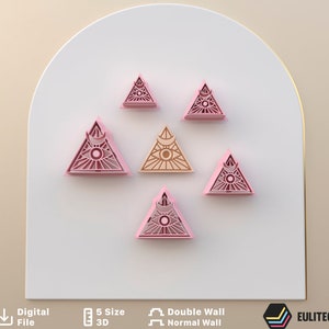 Op de afbeelding: Vijf roze en één beige plastic koekjesvormen in de vorm van een driehoek met een oog- en halvemaanontwerp. De vormen zijn in piramidevorm gerangschikt op een wit oppervlak.