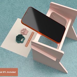 Peut inclure: Un support de téléphone rose avec un smartphone noir et une carte blanche avec deux emporte-pièces en forme de coquillage. La carte porte le texte "DIGITAL DOWNLOAD". L'image comprend également le texte "Digital STL Included".