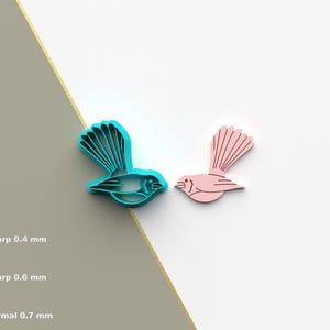 Puede incluir: Dos cortadores de galletas, uno azul y otro rosa, con forma de pájaros con las alas extendidas. El pájaro azul está a la izquierda y el pájaro rosa está a la derecha.