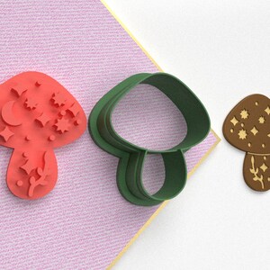 Pode incluir: Tr&ecirc;s cortadores de biscoitos em forma de cogumelo. Um &eacute; vermelho com um desenho de lua e estrelas, outro &eacute; verde e o &uacute;ltimo &eacute; marrom com um desenho de lua e estrelas.