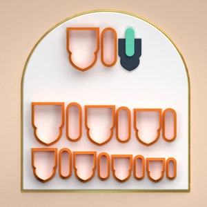 Può includere: Un set di 12 tagliabiscotti in plastica arancione di varie forme, tra cui archi, ovali e scudi. I tagliabiscotti sono disposti in tre file su uno sfondo bianco con un bordo dorato.