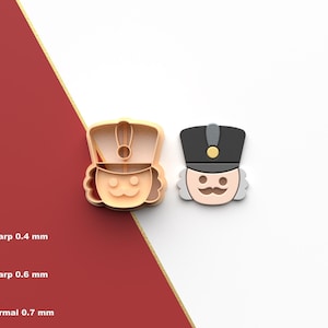 Puede incluir: Dos cortadores de galletas con temática de cascanueces. Uno es un cortador de plástico marrón claro, y el otro es una cabeza de cascanueces terminada. La imagen también muestra el icono del archivo STL y las opciones de grosor del cortador: Sharp 0,4 mm, Sharp 0,6 mm y Normal 0,7 mm.