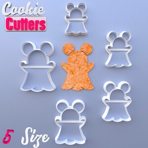 Puede incluir: Un conjunto de cortadores de galletas de plástico blanco con forma de fantasma con orejas de ratón, junto con una galleta con forma de fantasma naranja. La imagen incluye el texto "Cookie Cutters" y "5 Size" en una fuente lúdica, sobre un fondo azul claro.