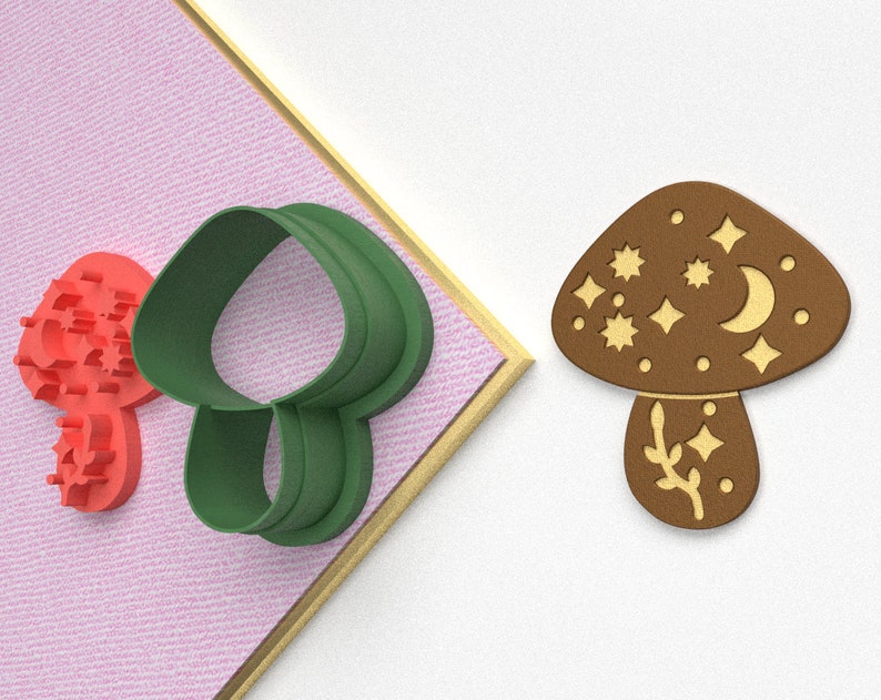 Pode incluir: Um conjunto de dois cortadores de biscoitos, um vermelho e outro verde. O cortador verde tem a forma de um cogumelo com uma parte superior arredondada e um caule. O cortador vermelho tem a forma de uma estrela com um desenho de estrela de cinco pontas.