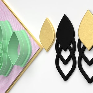 May include: A set of three green plastic cookie cutters shaped like a leaf with a decorative pattern. The cutters are shown next to two pairs of earrings, one pair is black and the other is gold.
