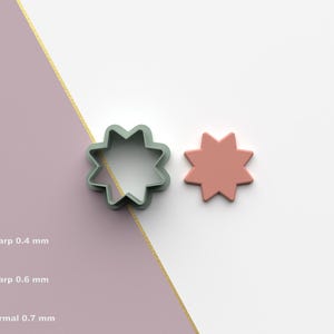 Puede incluir: Dos objetos en forma de estrella. Uno es un cortador de galletas verde claro, y el otro es una estrella de color coral sólido. Los objetos están sobre un fondo blanco y rosa con una línea diagonal dorada. La imagen también incluye texto y un icono STL.