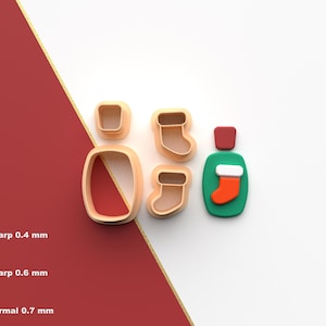 Puede incluir: Un conjunto de cortadores de galletas con temática navideña en varias formas, incluyendo una botella, un calcetín y formas rectangulares y cuadradas. Los cortadores son de color beige, rojo, verde y blanco. La imagen también incluye texto.