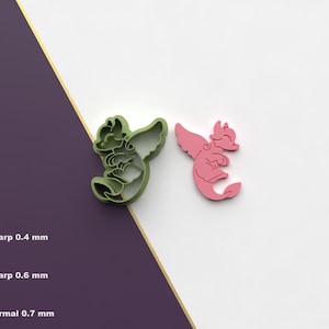 Puede incluir: Dos cortadores de galletas con forma de dragón, uno verde y otro rosa, se muestran sobre un fondo blanco y morado. Los cortadores tienen alas y diseños detallados. La imagen también muestra opciones de borde de corte: Sharp 0,4 mm, Sharp 0,6 mm y Normal 0,7 mm.