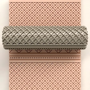 Puede incluir: Un rodillo de patrón gris con un diseño de diamantes y puntos. El rodillo se coloca sobre un fondo rosa con un patrón geométrico repetitivo. Adecuado para manualidades y proyectos decorativos.