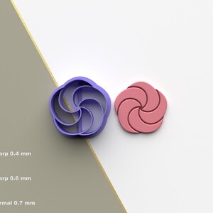 Puede incluir: Un cortador de galletas de plástico morado con forma de flor junto a una galleta rosa con forma de flor. El cortador tiene un diseño en espiral. La imagen también muestra un diagrama del filo del cortador: 0,4 mm, 0,6 mm y 0,7 mm.
