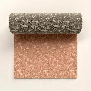 Puede incluir: Dos rollos de tela estampada. El rollo superior es gris oscuro con un diseño de hojas. El rollo inferior es de color melocotón claro con un patrón de hojas similar. La tela tiene una apariencia texturizada.