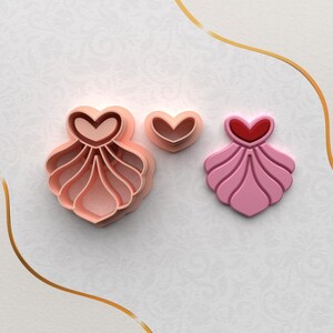 May include: A set of three pink and red heart-shaped cookie cutters. The largest cutter is a layered design with a heart shape in the center. The medium cutter is a simple heart shape. The smallest cutter is a layered design with a heart shape in the center.