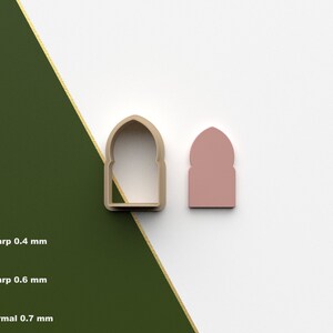 Puede incluir: Un cortador de galletas impreso en 3D con forma de puerta arqueada con la parte superior puntiaguda. El cortador está hecho de plástico marrón y se muestra junto a una versión de plástico rosa del mismo diseño.