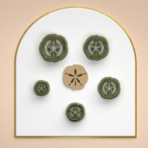 May include: A set of six cookie cutters in the shape of seashells. The cutters are green and brown and are arranged on a white surface.