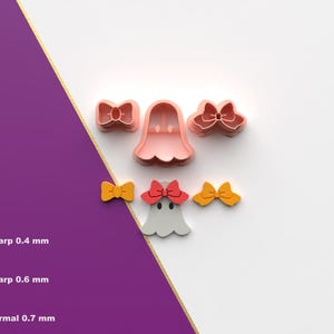 Puede incluir: Un conjunto de cortadores de galletas en forma de lazos y un fantasma. Los cortadores son rosas, amarillos y rojos. El cortador de fantasma tiene un lazo rojo. La imagen también muestra los grosores de corte: 0,4 mm, 0,6 mm y 0,7 mm.