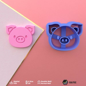 Op de afbeelding: Twee koekjesvormen in de vorm van een varken, een roze en een blauwe. De roze vorm is massief, terwijl de blauwe vorm hol is. Beide vormen hebben hetzelfde ontwerp, met een varkensgezicht met oren, ogen en een snuit.