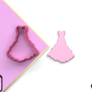 May include: Two pink plastic cookie cutters shaped like a dress. The cutters are on a pink and gold background. The image also includes a file icon labelled "STL".