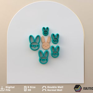 Peut inclure: Un ensemble de six emporte-pièces en forme de lapin bleu turquoise, dont un emporte-pièce en forme de lapin brun. Les emporte-pièces sont disposés en cercle sur un fond blanc.