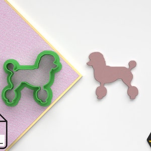 May include: Green plastic cookie cutter in the shape of a poodle with wheels. The cutter is on a pink and white patterned surface. A pink silhouette of a poodle with wheels is on a white surface.