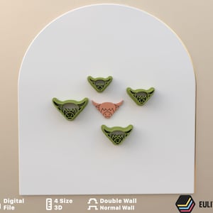 May include: Five 3D printed cookie cutters in the shape of a Highland cow head. Four are green and one is pink.