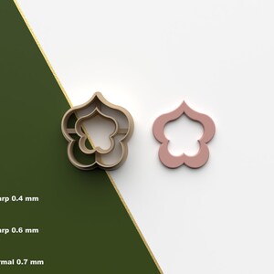 Puede incluir: Un cortador de galletas impreso en 3D con forma de flor de cinco pétalos. El cortador se muestra en dos colores diferentes: dorado y rosa. La imagen también muestra las diferentes opciones de grosor para el cortador: Sharp 0.4 mm, Sharp 0.6 mm y Normal 0.7 mm.