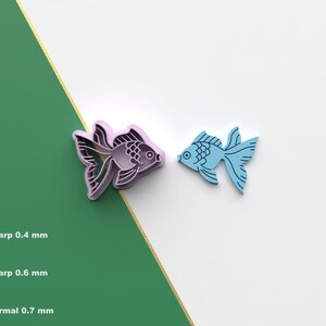 May include: Two fish-shaped objects, one lavender and one light blue, are displayed against a white and green background. The lavender fish has detailed fins and scales. The light blue fish has a simpler design. The image includes an STL file icon.