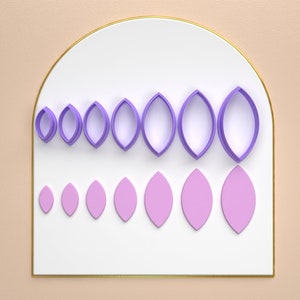 Puede incluir: Un juego de 10 cortadores de galletas en forma de hoja de color morado y rosa de diferentes tamaños, dispuestos en orden de menor a mayor sobre una superficie blanca con un borde dorado.