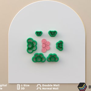 Può includere: Set di sei tagliapasta in plastica verde a forma di fiori. I tagliapasta sono disposti in cerchio con un tagliapasta a forma di fiore rosa al centro.