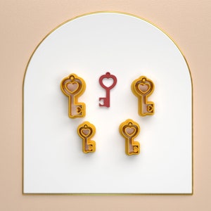 May include: Five gold-coloured key-shaped charms with heart-shaped keyholes. One charm is red.